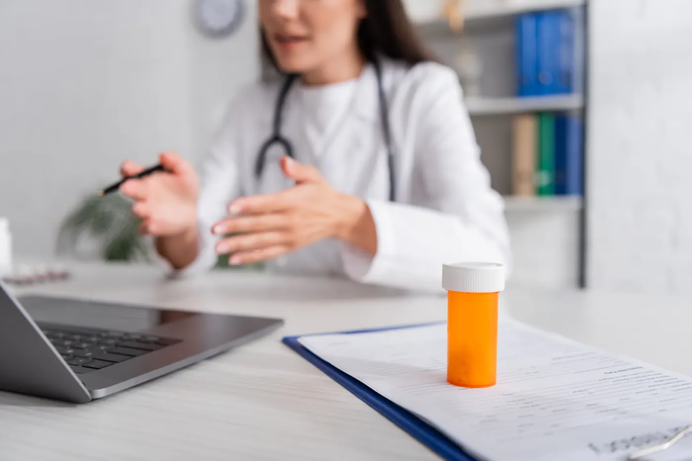 Clinician at a desk with a laptop and a bottle of prescription medication on a clipboard